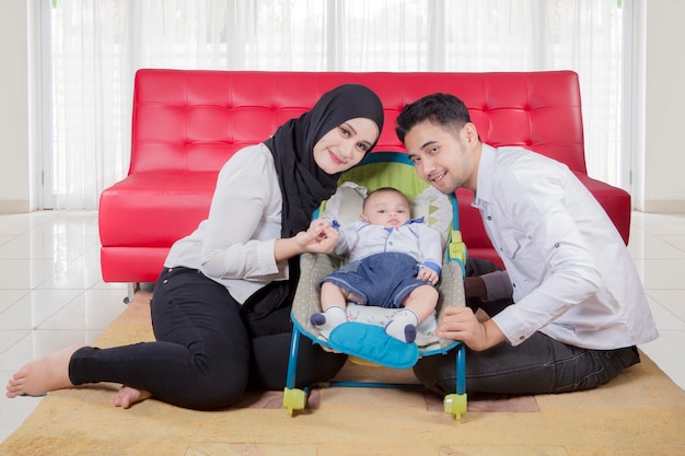 Happy family of father mother and baby boy posing in front of sofa