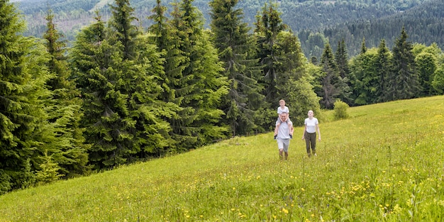 Happy family: father with son on shoulders and mother go on a green field