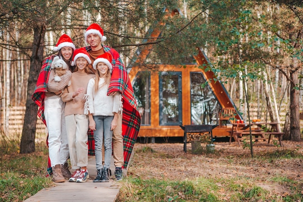 Happy family of four in Santa hat enjoying Christmas vacation. Parent with kids wrapped in a blanket