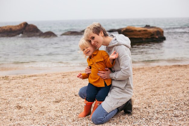 Happy family friends forever concept Smiling mother and little son playing together near sea in autumn time