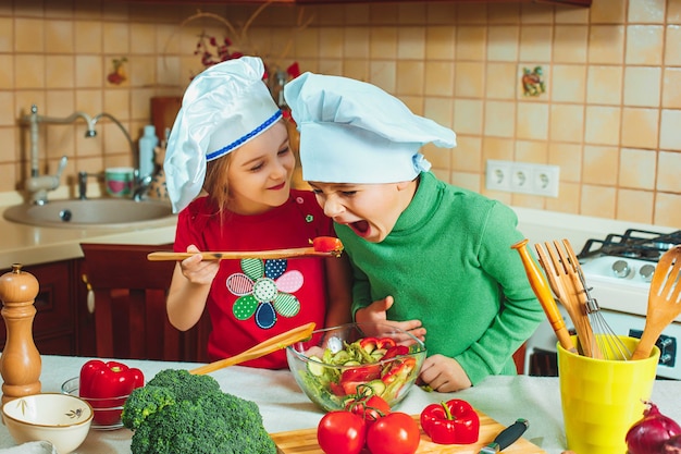 Happy family funny kids are preparing the a fresh vegetable salad in the kitchen