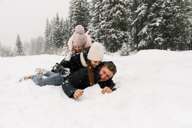 Happy family have fun in winter forest. Mother, father and dauther lie on the ground and playing with snow. Family concept. Enjoying spending time together