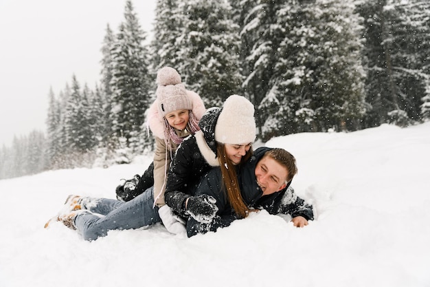 Happy family have fun in winter forest. Mother, father and dauther lie on the ground and playing with snow. Family concept. Enjoying spending time together