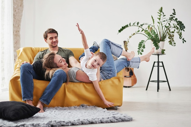 Happy family have fun on the yellow sofa in the living room of their new house.