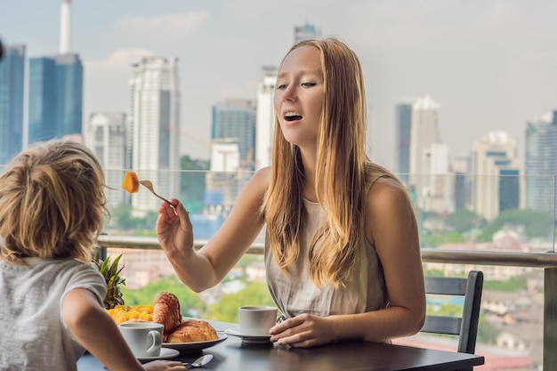 Happy family having breakfast on the balcony. Breakfast table with coffee fruit and bread croisant on a balcony against the backdrop of the big city