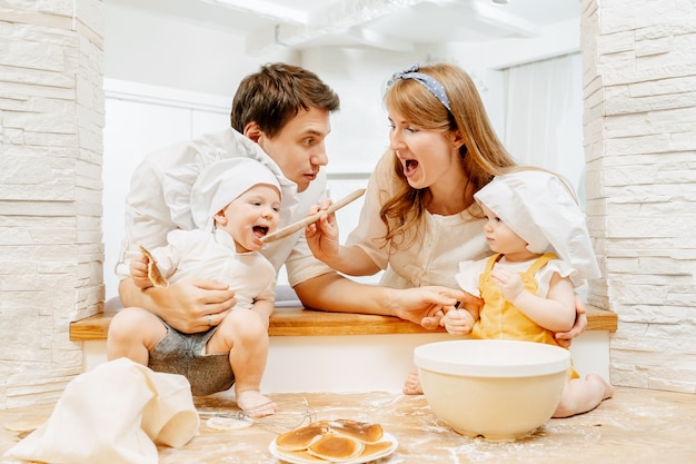 Happy family having fun at home on the background of the kitchen prepares sweet pastries. Soiled children with flour laugh with mom and dad.