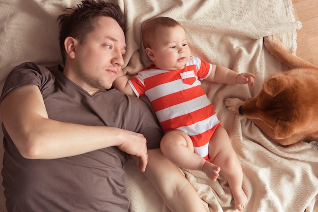 Happy family having fun with cute Shiba Inu dog. Father with his smiling baby son and Shiba Inu pet at home, top view