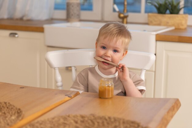 Happy family at home Baby boy feeding himself in kitchen Little boy with messy funny face eats healthy food Child learns eat by himself holding spoon Self feeding