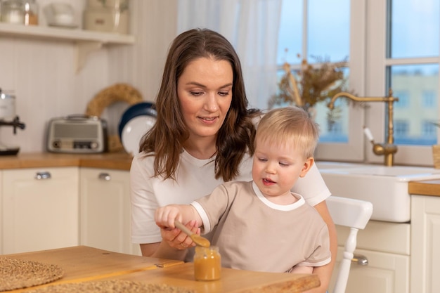 Happy family at home mother feeding baby in kitchen little boy with messy funny face eats healthy fo