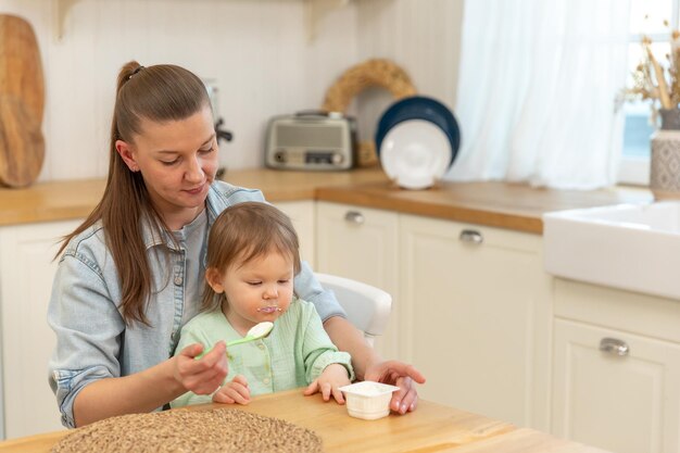 Happy family at home mother feeding her baby girl from spoon in kitchen little toddler child with me