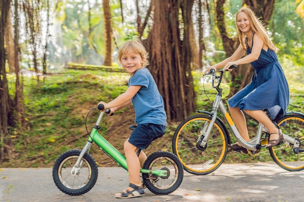 Happy family is riding bikes outdoors and smiling. Mom on a bike and son on a balancebike