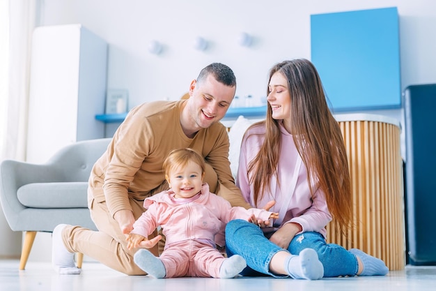 Happy family is sitting on the floor with their little child th