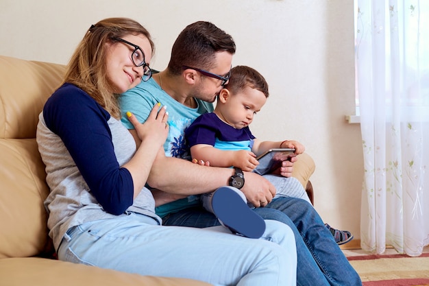 Happy family is sitting with a tablet in the room on the couch