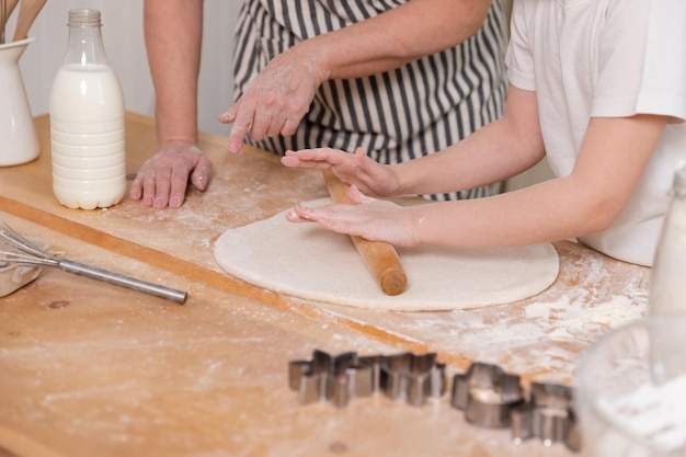 Happy family in kitchen grandmother granddaughter child hands roll out dough on kitchen table togeth