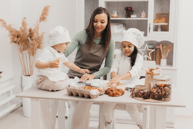 Happy family in the kitchen. mom and children in cook costumes in the kitchen. mom and children prepare dough, bake cookies