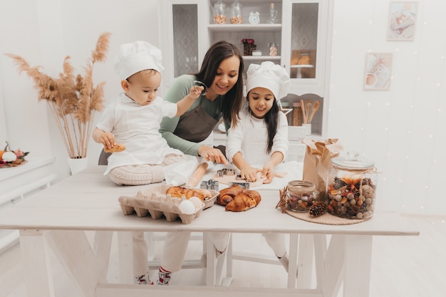 Happy family in the kitchen. mom and children in cook costumes in the kitchen. mom and children prepare dough, bake cookies