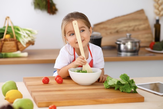 Happy family in the kitchen Mother and child daughter cooking tasty breakfest of fresh salad Little helper slicing and mix tomatos and greenery