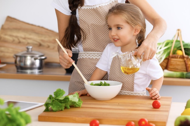 Happy family in the kitchen Mother and child daughter cooking tasty breakfest of fresh salad Little helper slicing and mix tomatos and greenery