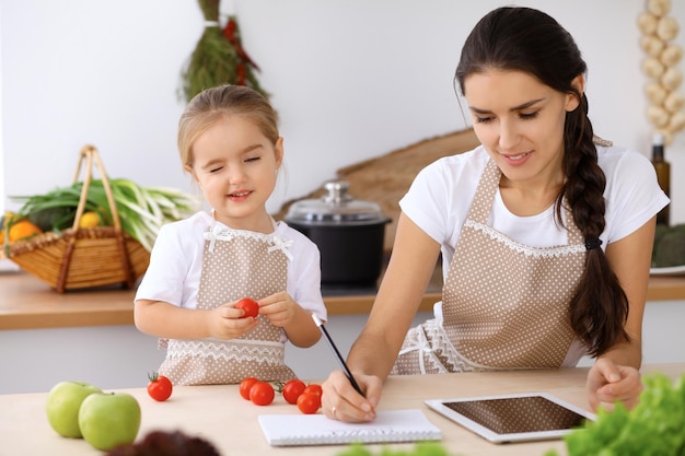 Happy family in the kitchen Mother and child daughter make menue for cooking tasty breakfest in the kitchen Little helper is ready for houshold job