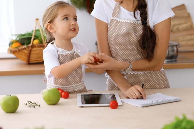 Happy family in the kitchen Mother and child daughter make menue for cooking tasty breakfest in the kitchen Little helper is ready for houshold job