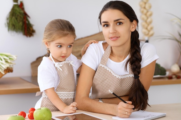 Happy family in the kitchen Mother and child daughter make menue for cooking tasty breakfest in the kitchen Little helper is ready for houshold job