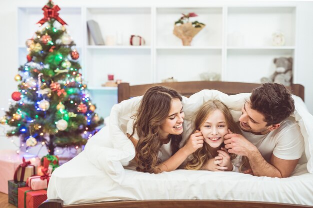 The happy family lay and fun on the bed near the christmas tree