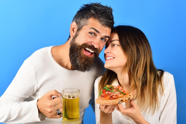 Happy family, lovable couple enjoying pizza together. Leisure, food and drinks, love concept - husband and wife eating pizza. Smiling happy man and woman. Couple laughing and eating pizza, drinks beer