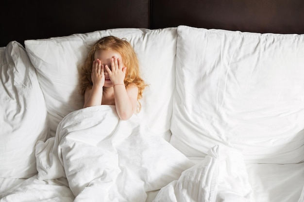 Happy family lying under blanket in bed at home