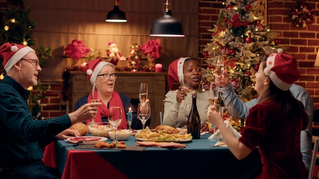 Happy family members drinking champagne while celebrating winter holiday together. Cheerful festive people singing traditional songs while enjoying Christmas dinner at home.