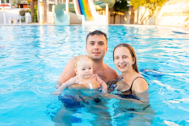 Happy family mom dad and baby daughter are swimming in the pool with water slides and having fun on vacation