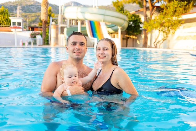 Happy family mom dad and baby daughter are swimming in the pool with water slides and having fun on vacation