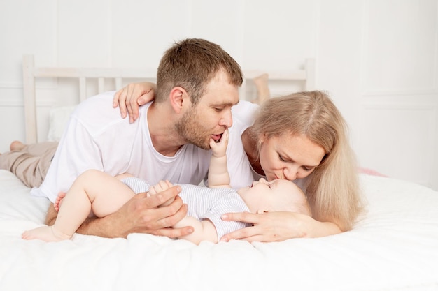 Happy family mom dad and baby play on the bed at home and have fun