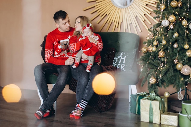 Happy family mom dad and little daughter in red traditional Christmas clothes spending time together near Christmas tree copy space