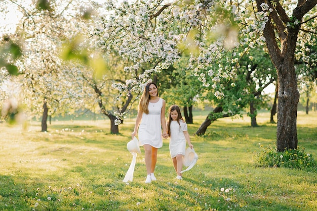 Happy family mom and daughter in a blooming apple orchard holding hands and walking in the park in spring