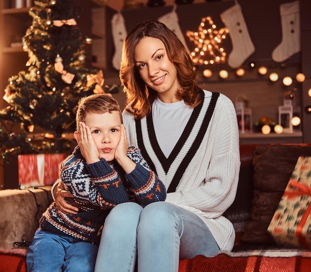 Happy family. Mom hugging her cute little boy while sitting on sofa in decorated room during Christmas time.