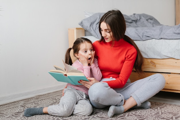 Happy family mother and child daughter reading holding book lying in bed