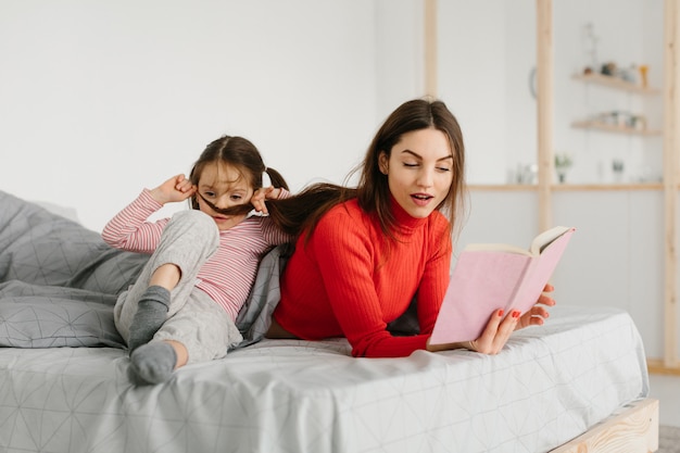 Happy family mother and child daughter reading holding book lying in bed