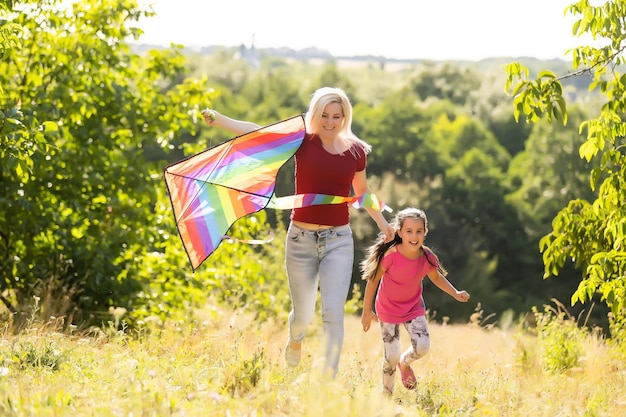 happy family mother and child run on meadow with a kite in the summer on the nature