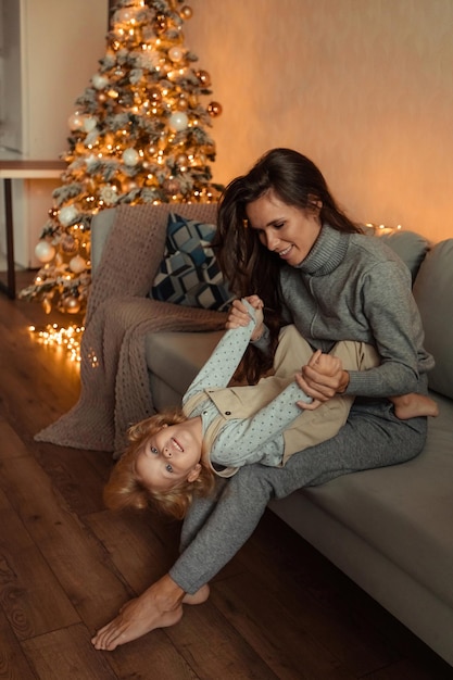 Happy family mother and daughter at home near Christmas tree waiting for New Year