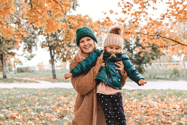 Happy family mother and daughter is in autumn city park They posing smiling playing and having fun Bright yellow trees