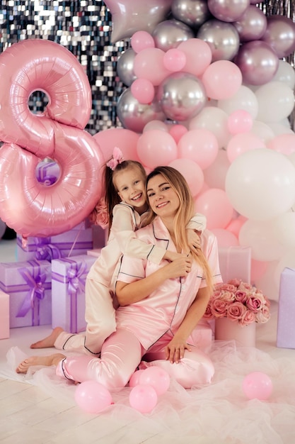 Happy family mother and daughter in pajamas with balloons celebrate the childs birthday