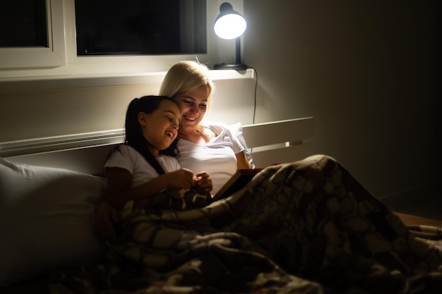 happy family mother and daughter read a book in the evening at home