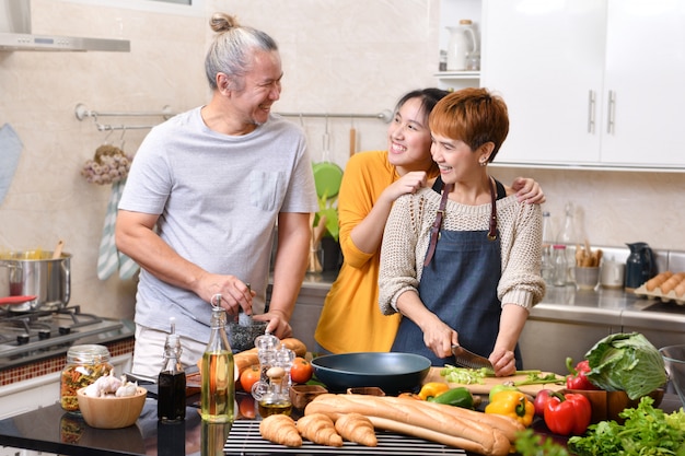 Happy family of mother father and daughter cooking in kitchen making healthy food together feeling fun