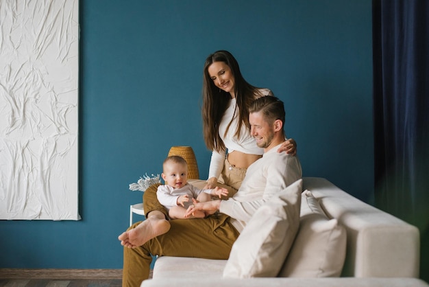 Happy family mother and father with a child at home in a blue room with a white sofa