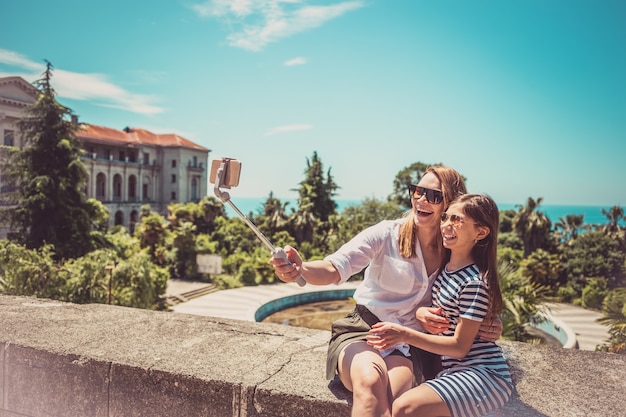 Happy family mother and her adorable little daughter on summer vacation taking selfie with smartphone