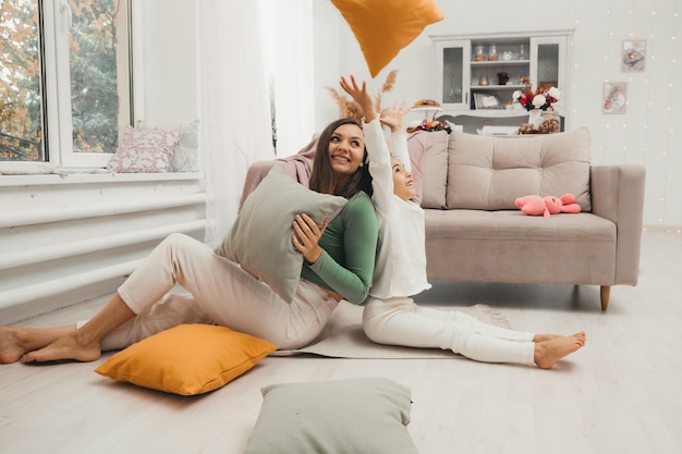 Photo a happy family! mother and her little daughter girl fight pillows on the floor near the sofa. happy family games.