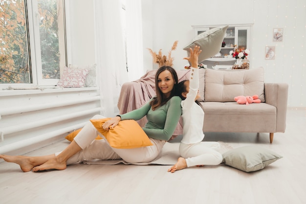 A happy family! Mother and her little daughter girl fight pillows on the floor near the sofa. Happy family games.