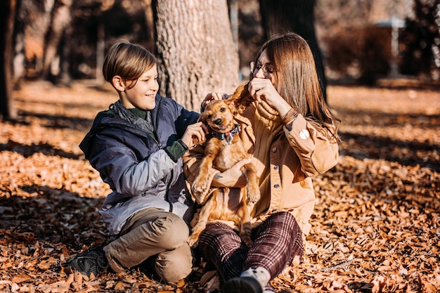 Happy family mother and teen boy son having fun with cocker spaniel puppy in autumn park