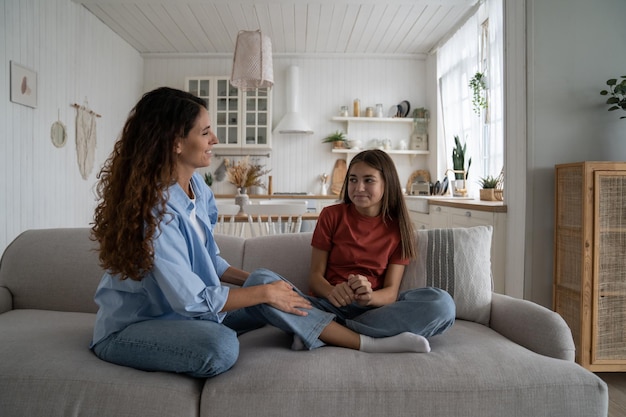 Happy family mother and teen girl daughter sitting on sofa bonding chatting having fun at home