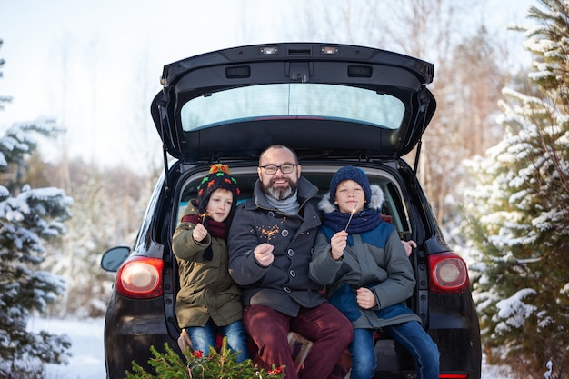 Happy family near black car at snowly winter day. Concept holiday vacation.